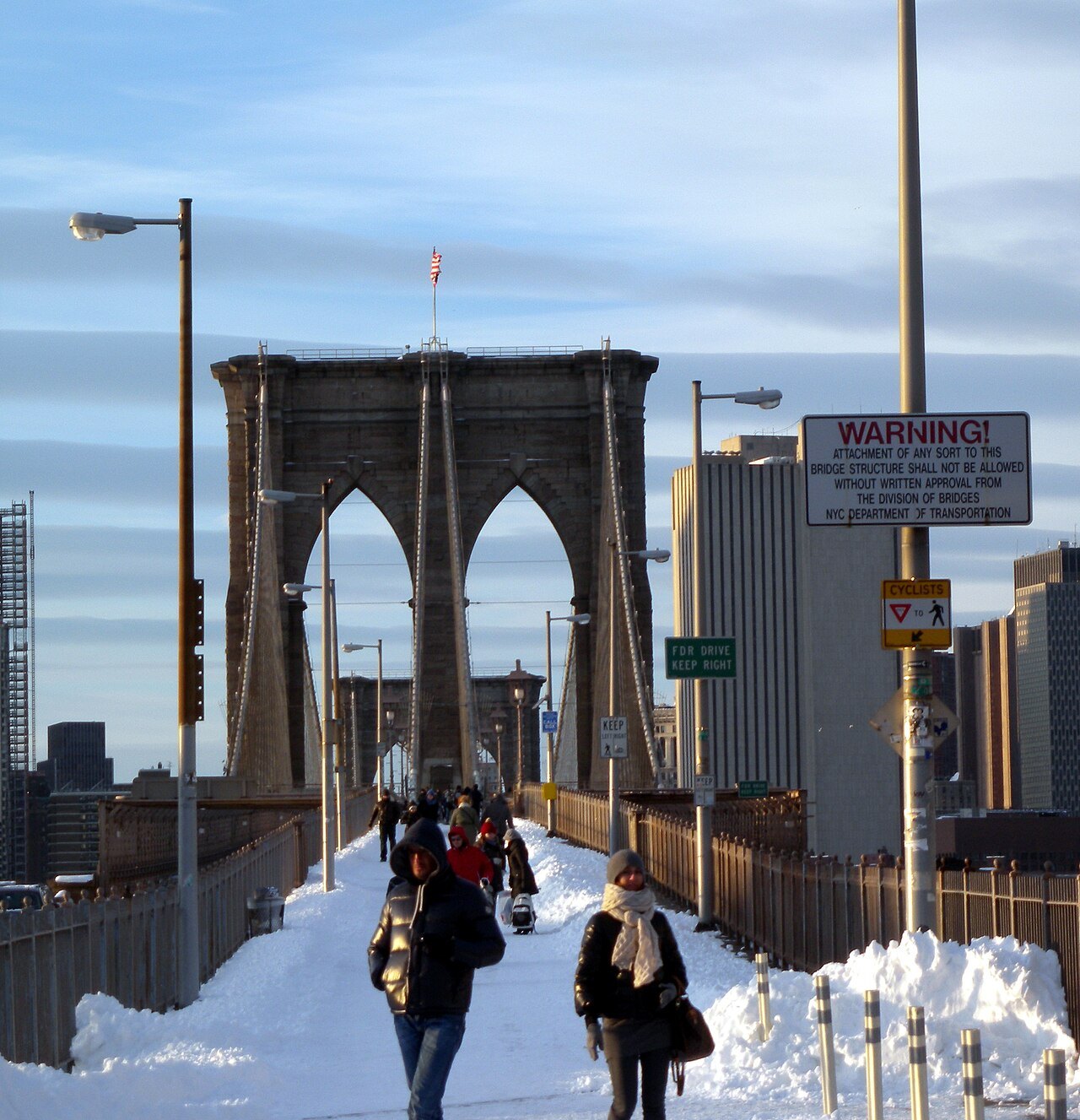 Walkers on the snow-covered promenade toward a Brooklyn Bridge tower