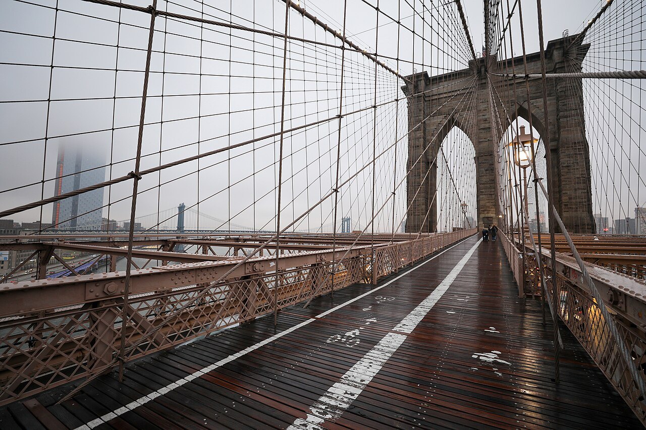 The empty promenade of the Brooklyn Bridge on a misty day, running toward a tower