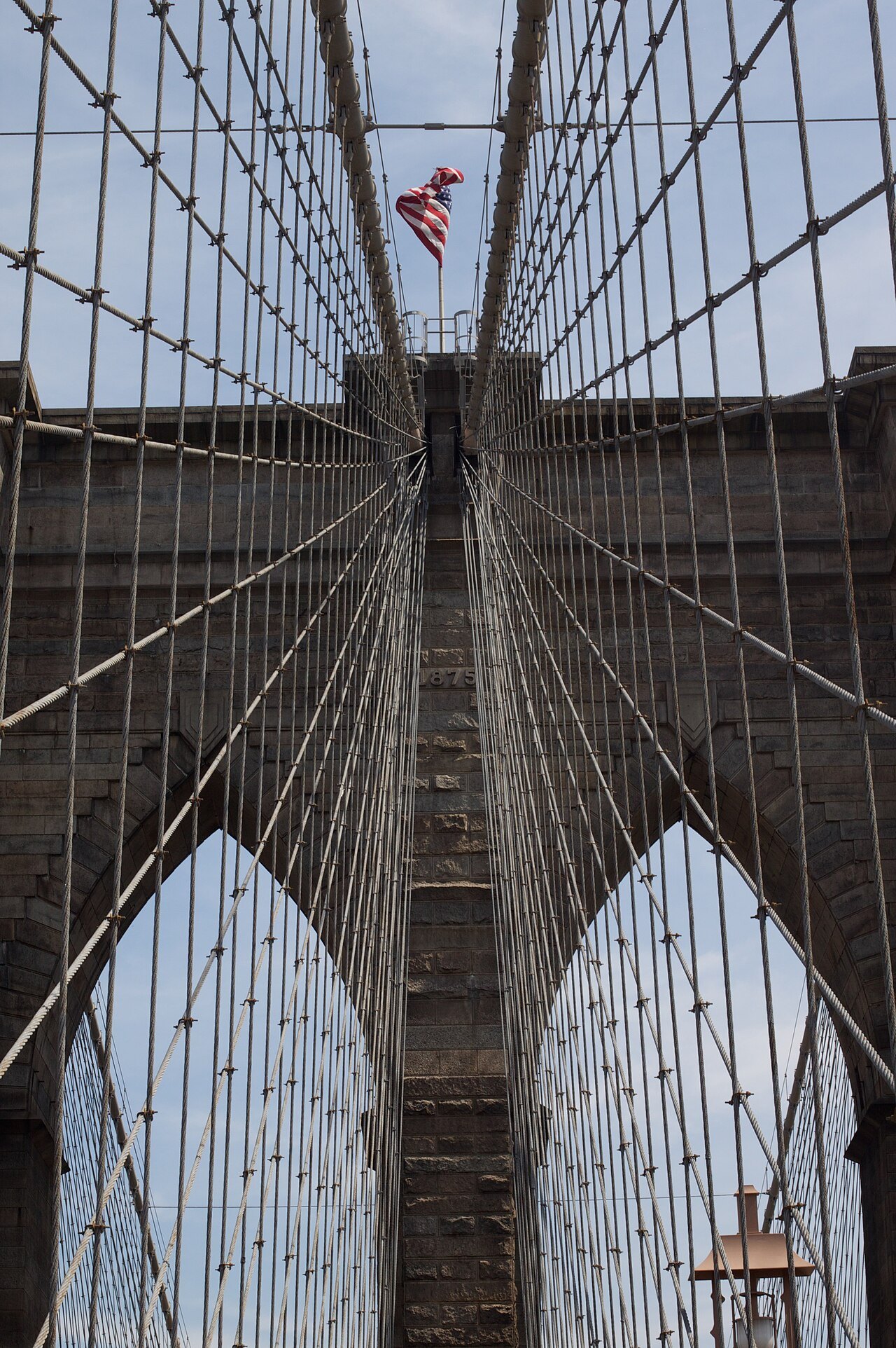 Looking straight up through the cables at a Gothic-arched tower of the Brooklyn Bridge