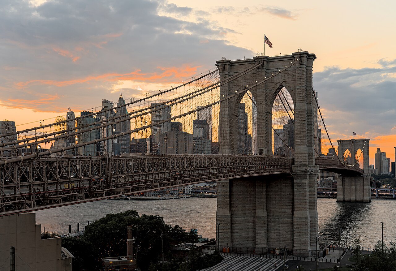 A Brooklyn Bridge tower at sunset, with the Lower Manhattan skyline behind the span