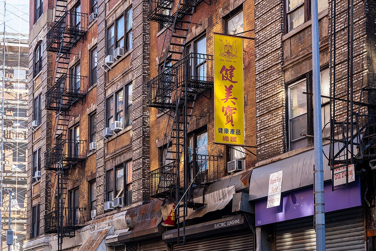 Tenements with fire escapes and a yellow sign on Mott Street