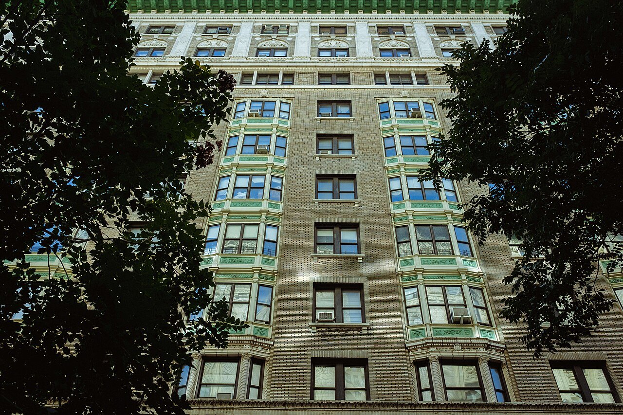 An Upper West Side apartment house with green bay windows, seen through trees