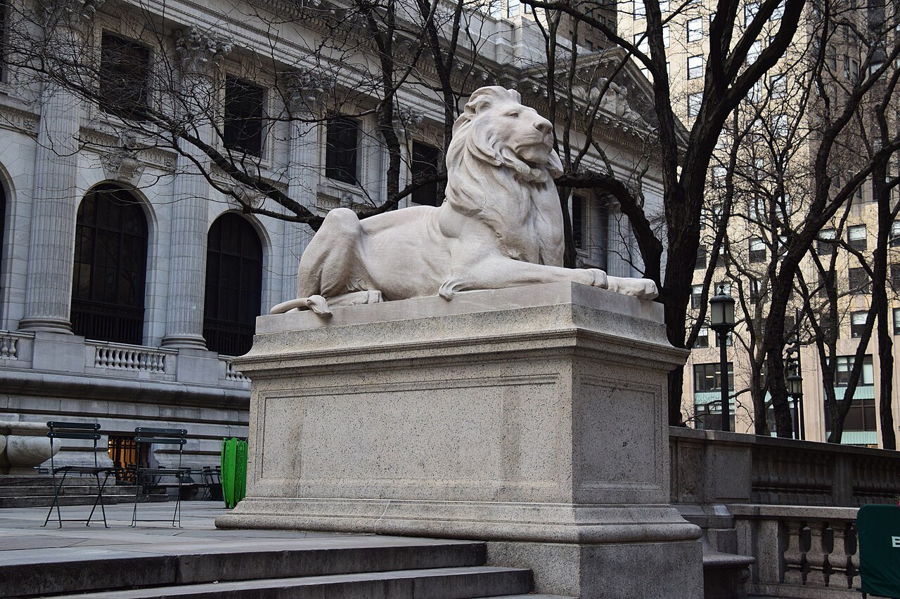 One of the library's marble lions on its pedestal, with bare winter trees