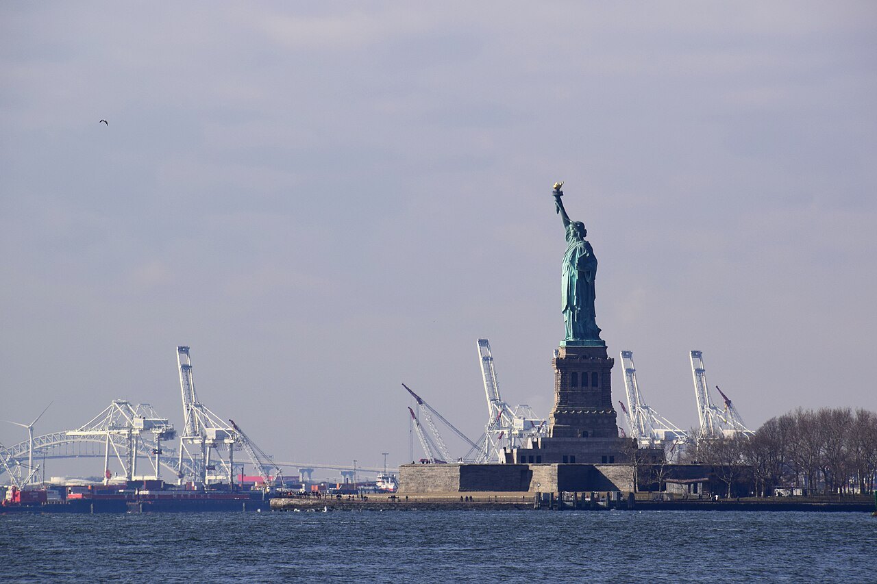 The Statue of Liberty with the cranes of the New Jersey port behind