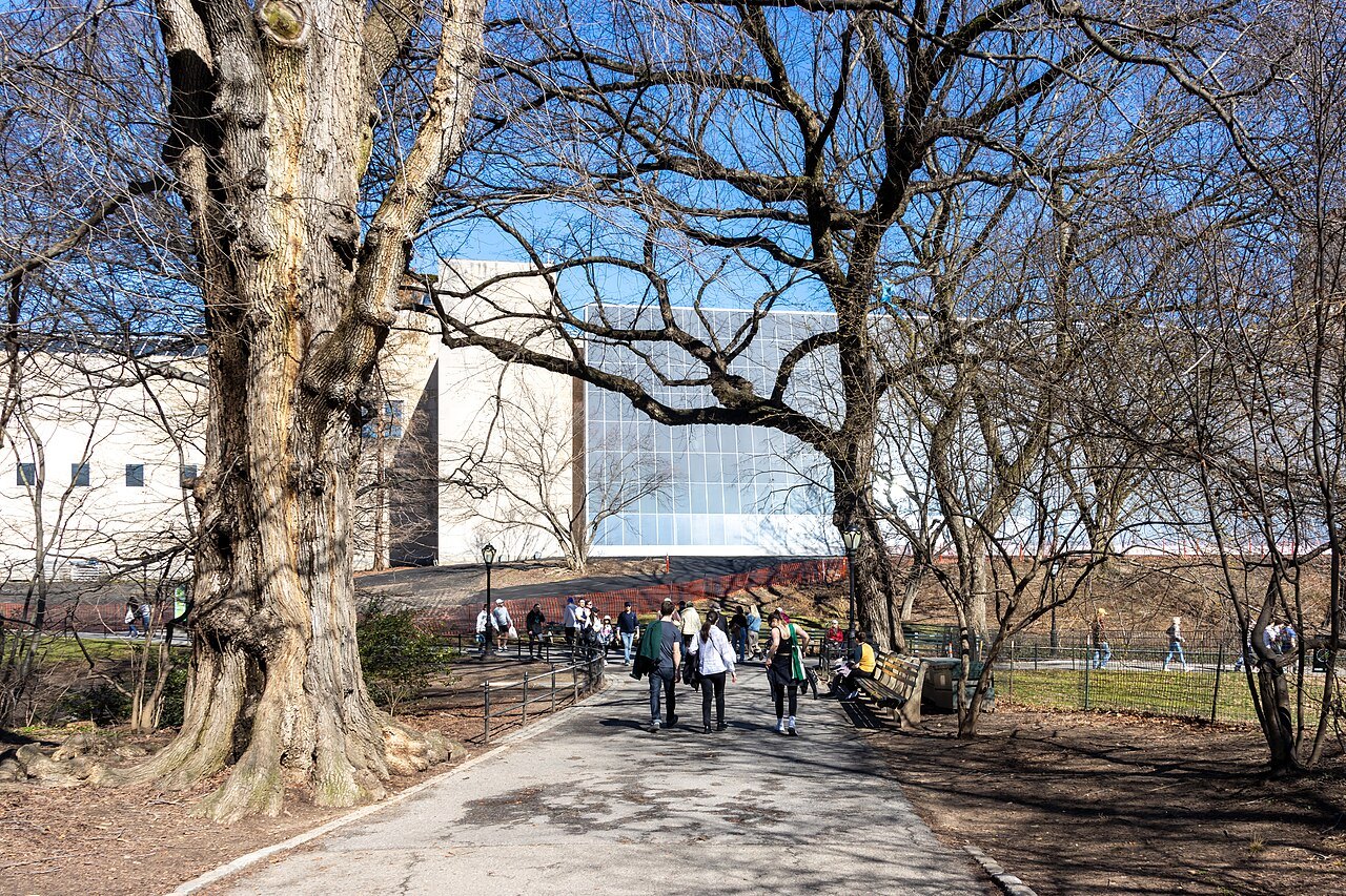 The Met's modern glass wing seen through the trees of Central Park