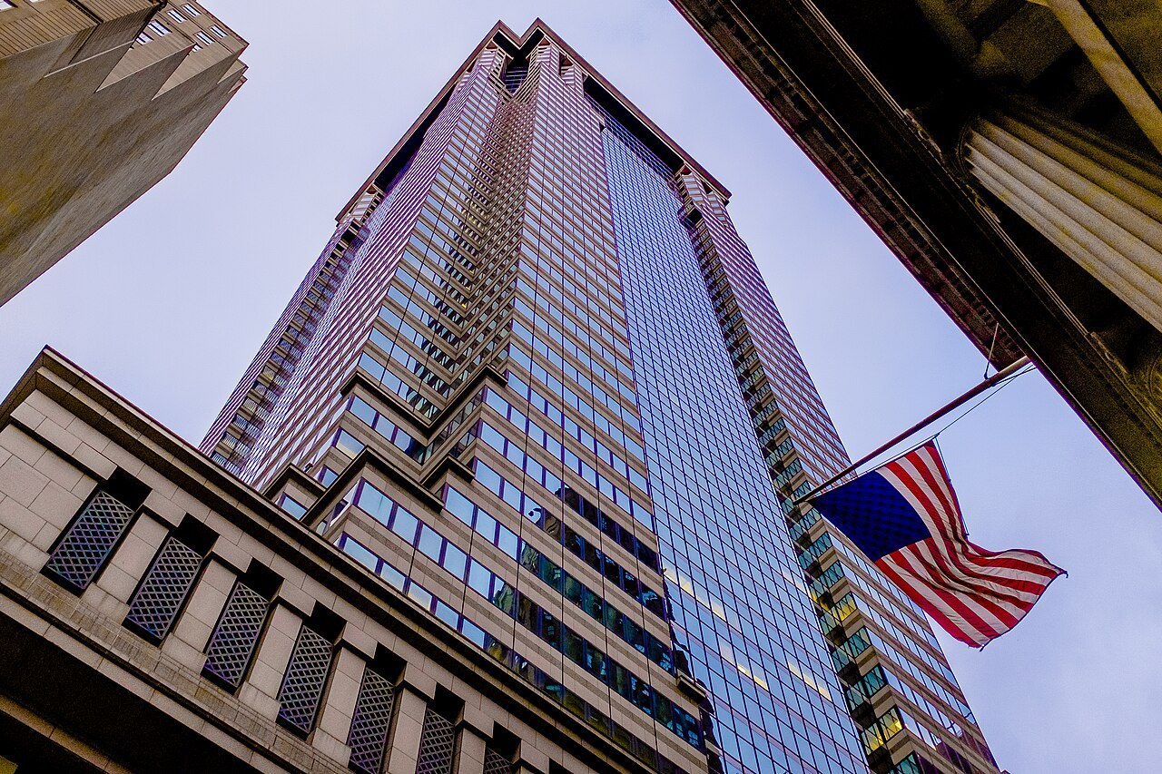 The tower of 60 Wall Street rising above the street, a flag in front
